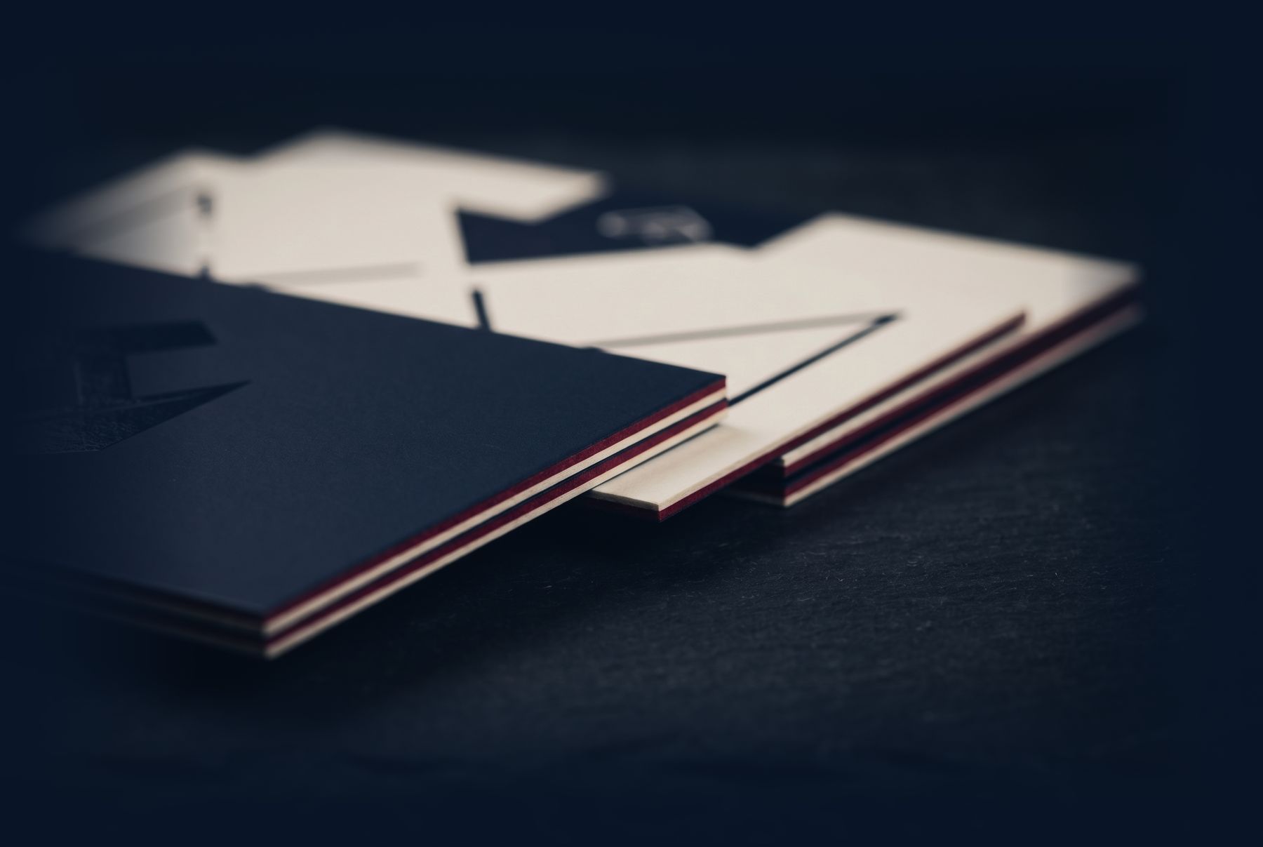 Stack of premium layered business cards in deep navy and warm cream on dark slate